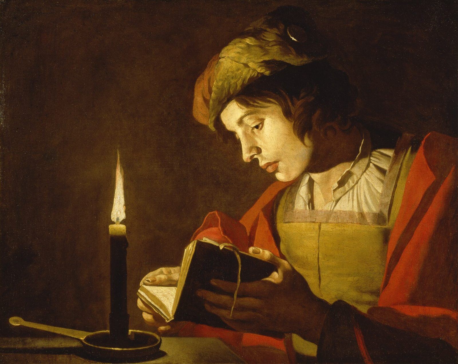 A young man reading a book by candlelight